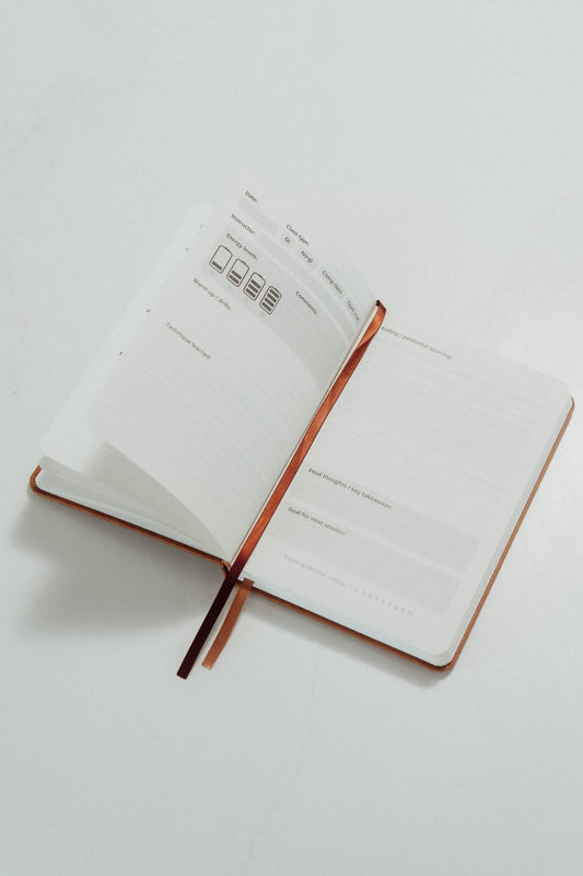 Open notebook with ivory pages and brown ribbon tabs and prompts to complete on a light gray background