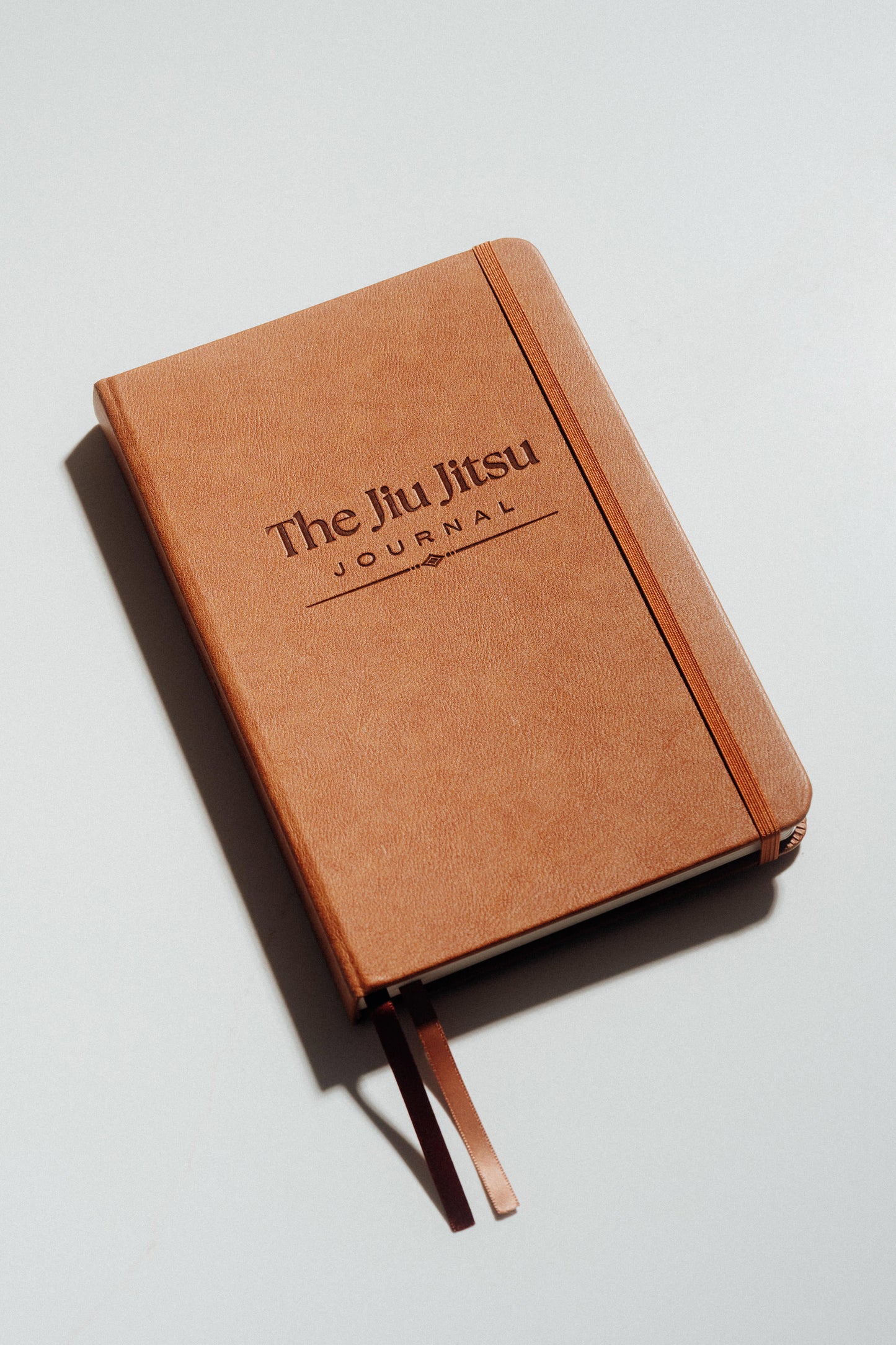 Brown notebook with 'The Jiu Jitsu Journal' debossed on the cover against a light grey background
