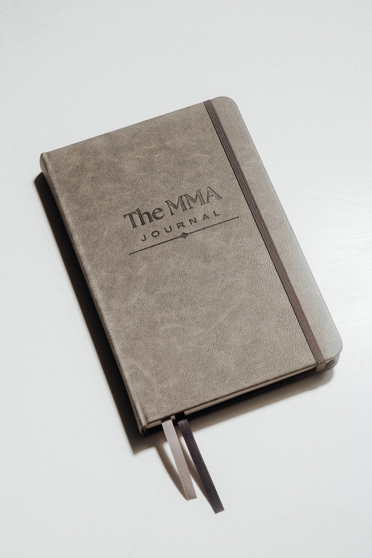 Grey notebook with 'The MMA Journal' debossed on the cover, on a light grey background