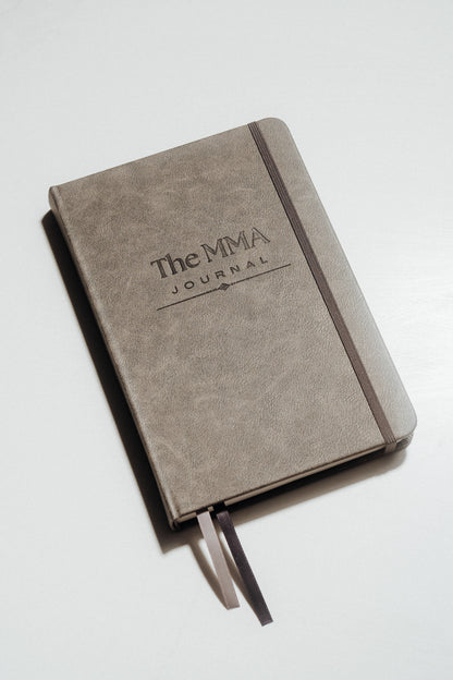 Grey notebook with 'The MMA Journal' debossed on the cover, on a light grey background