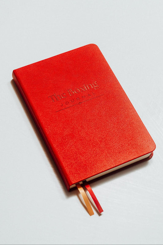 Red notebook with 'The Boxing Journal' debossed on the cover on a light grey background