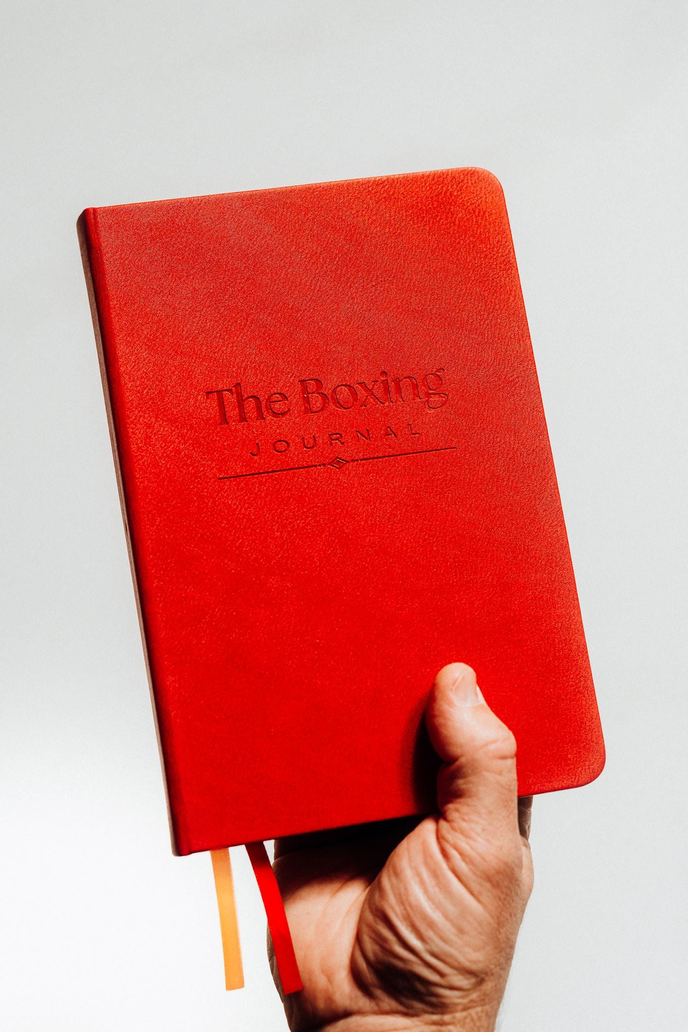 Red notebook titled 'The Boxing Journal' held by a hand against a light background