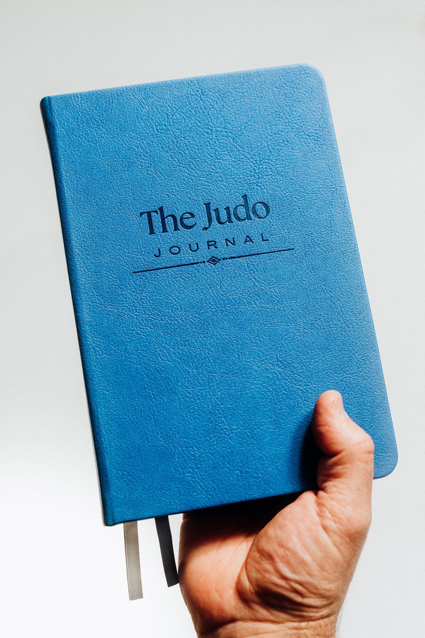 Blue notebook titled 'The Judo Journal' held by a hand against a light background