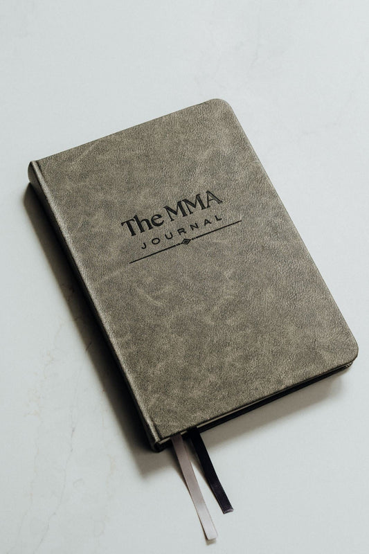Grey notebook with 'The MMA Journal' debossed on the cover, on a light grey background