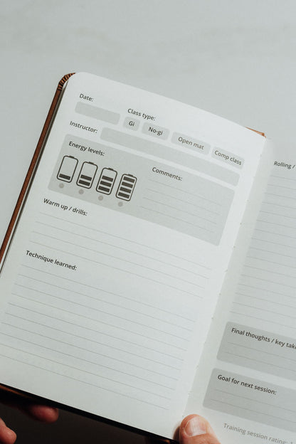 An open planner or notebook with lined pages and printed lesson-plan sections. Maint left page for bjj journal