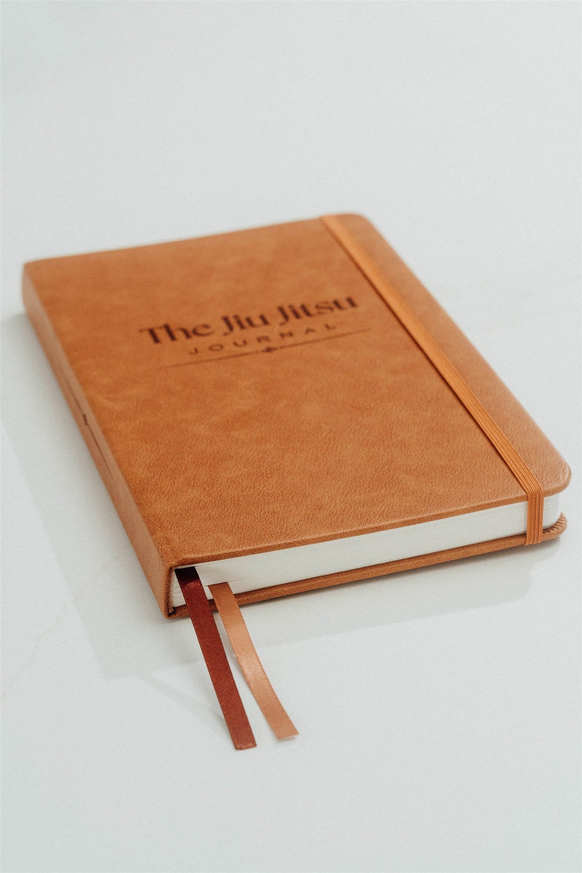 Brown leather journal with 'The Jiu Jitsu Journal' embossed on the cover showing ribbons on the notebook