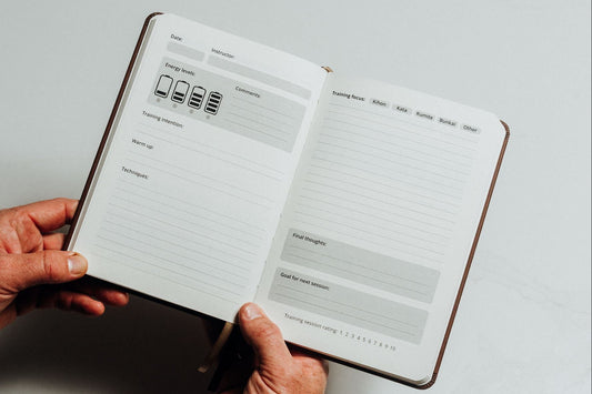 A person's hands holding open a slim hardcover planner or notebook with blank lined pages and simple gray printed sections.