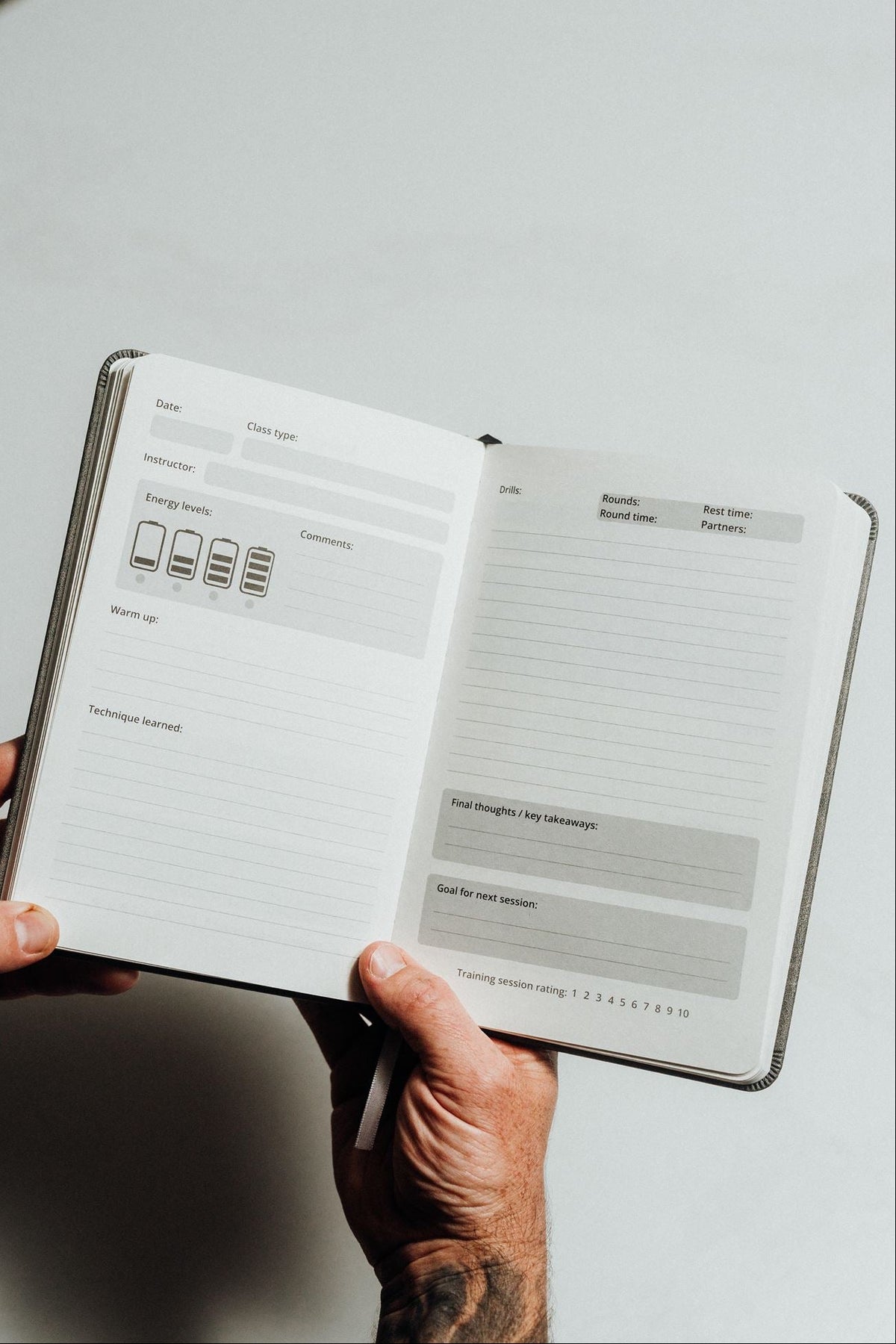 A person's hands holding an open minimalist planner or notebook with clean white pages featuring light gray lined sections and small icons.