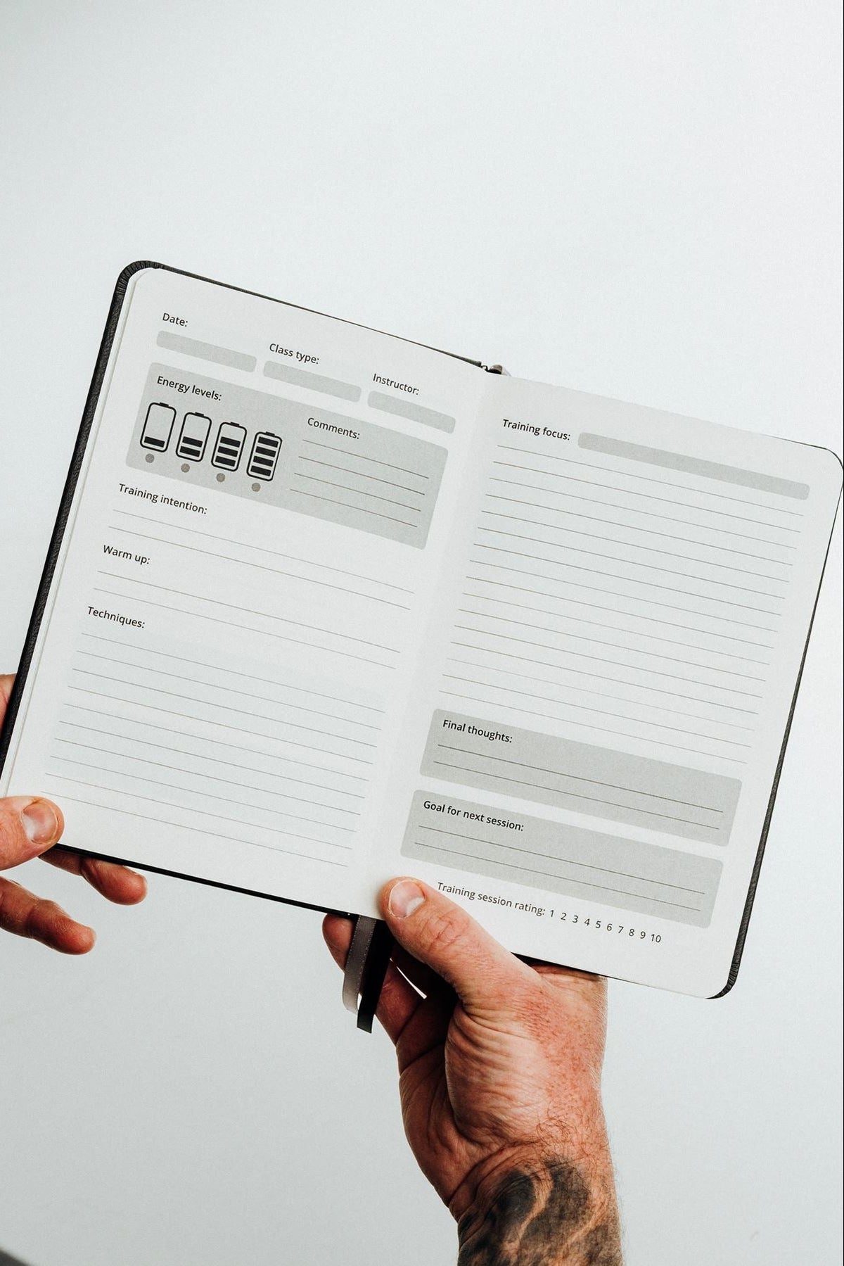 A person's hands holding an open black hardcover notebook or planner showing the main pages of the martial arts journal