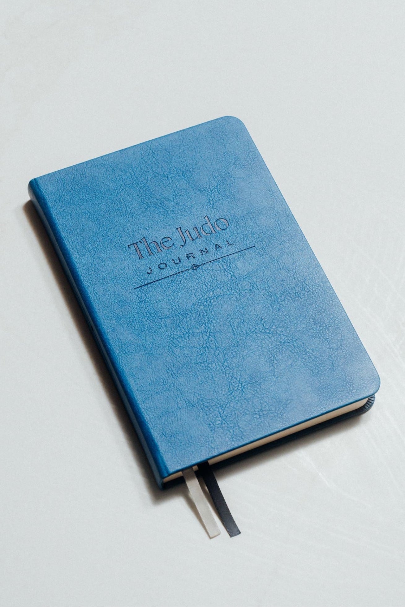Blue journal with 'The Judo Journal' debossed on it, on a light grey background